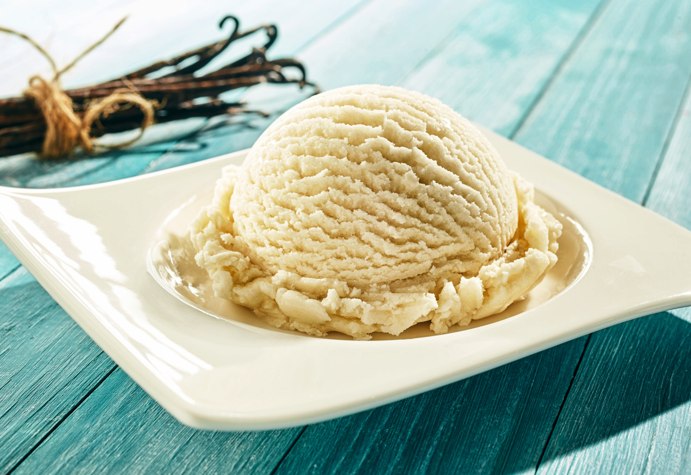 a scoop of vanilla ice cream one a small plate with a bundle of vanilla beans beside it