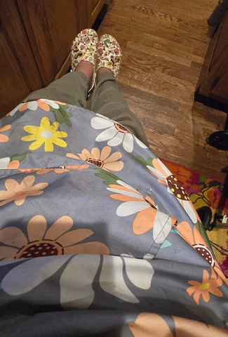 Looking down at a flower print apron and clogs from the perspective of the person wearing them