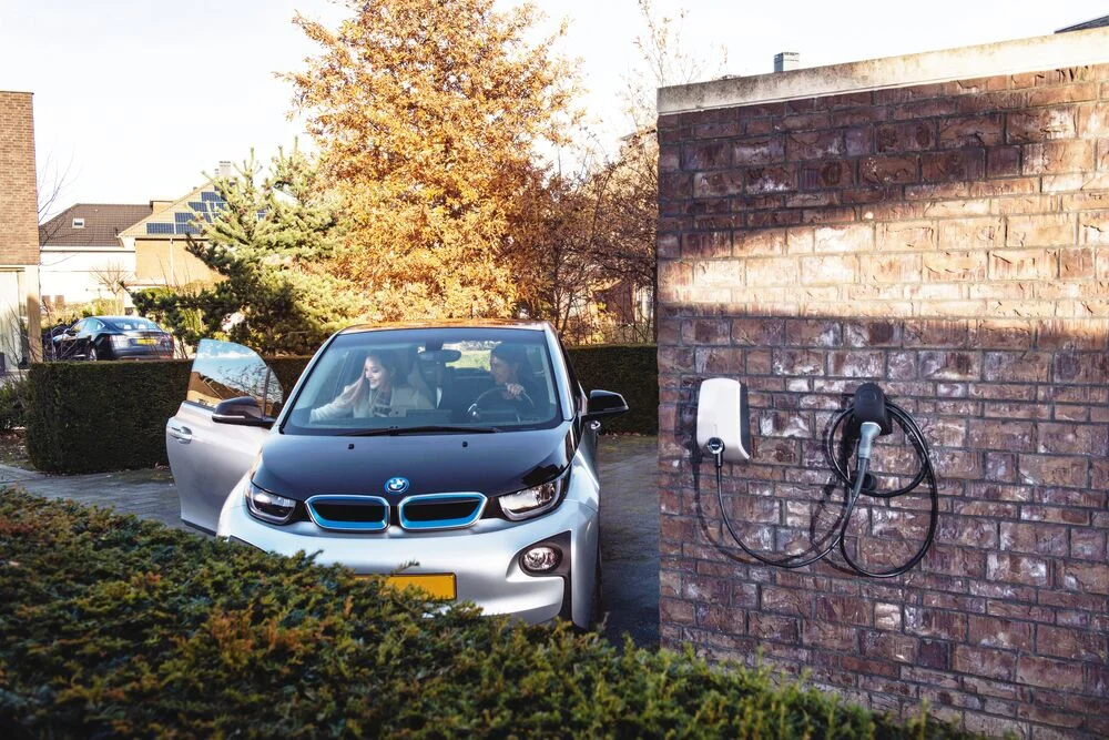A woman parking her electric car in the driveway, while another woman is getting out of the car