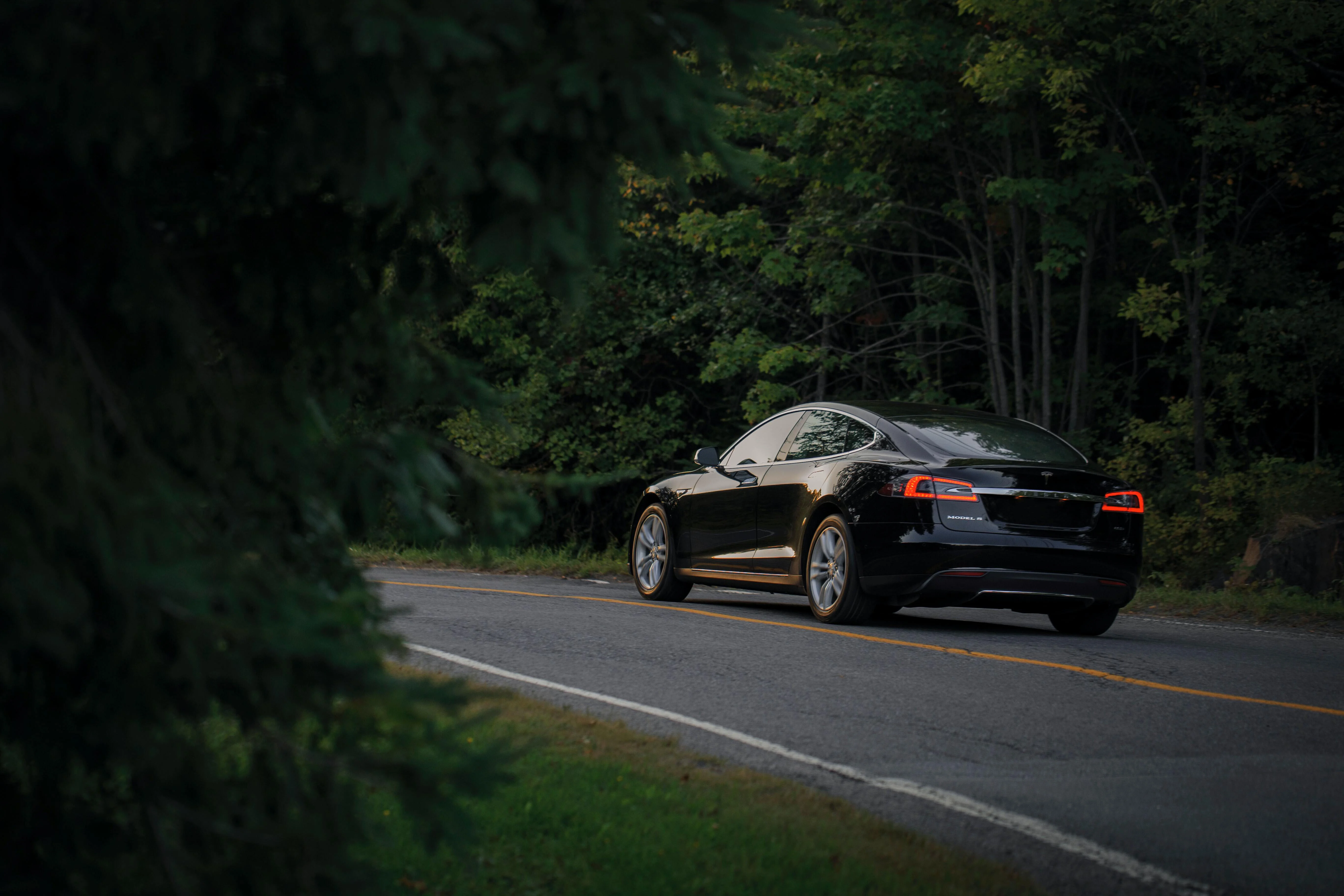 A modern electric vehicle driving on a road in the middle of a forest.