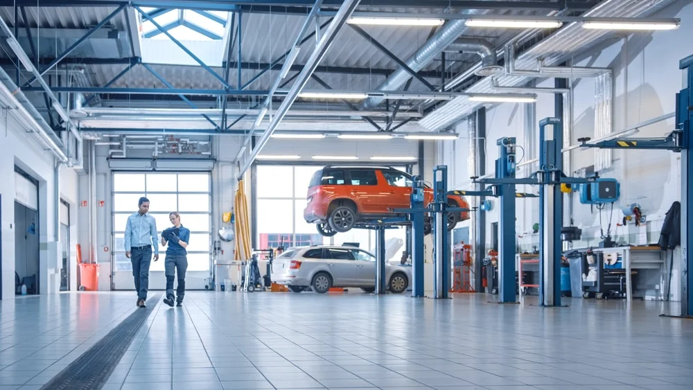 A repair shop showing cars being repaired and a mechanic explaining repairs on a digital tablet.
