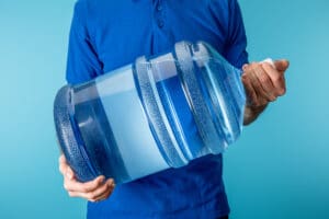Cropped view of courier holding bottled water isolated on blue Courier carrying a plastic water jug.
