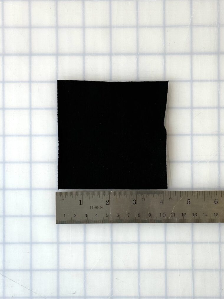 A square of black knit fabric measuring 4 inches by 4 inches. A silver ruler is placed beneath the fabric showing the measurement.