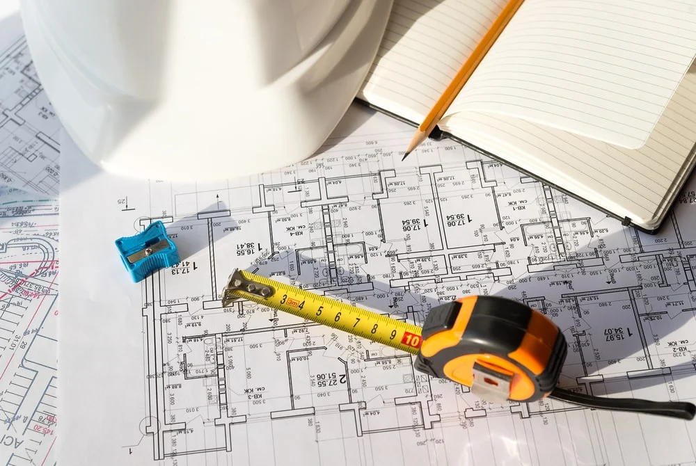 A blueprint of a location with a measuring tool and a notepad to plan upcoming construction work.