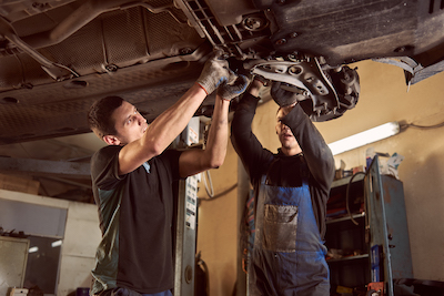 two auto mechanics checking underneath a car transmission