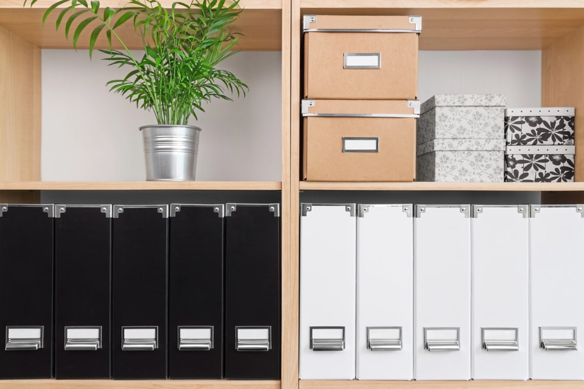 Home office storage ideas featuring neatly arranged binders, storage boxes, and a potted plant to create a functional and visually appealing workspace.