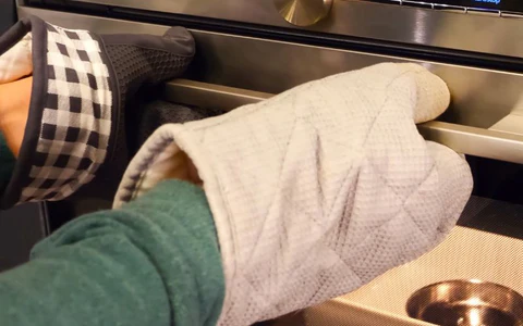 A person wearing oven mitts opening an oven door.