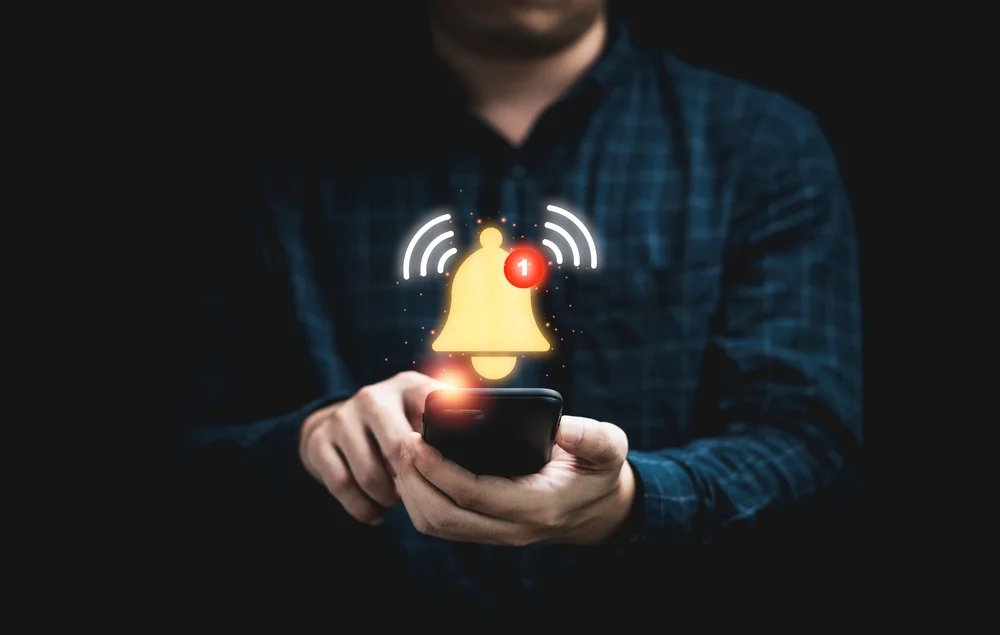 A closeup of a man holding a smartphone on which is displayed an alert notification.