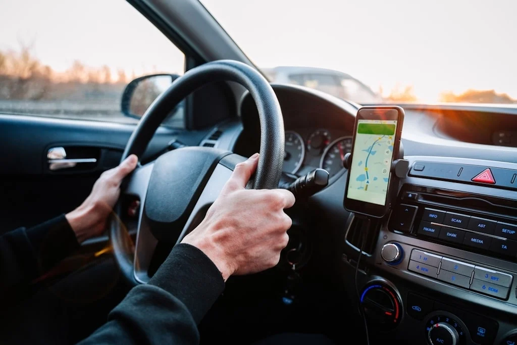 A view from inside an EV showing a man driving while checking his smartphone navigation app.
