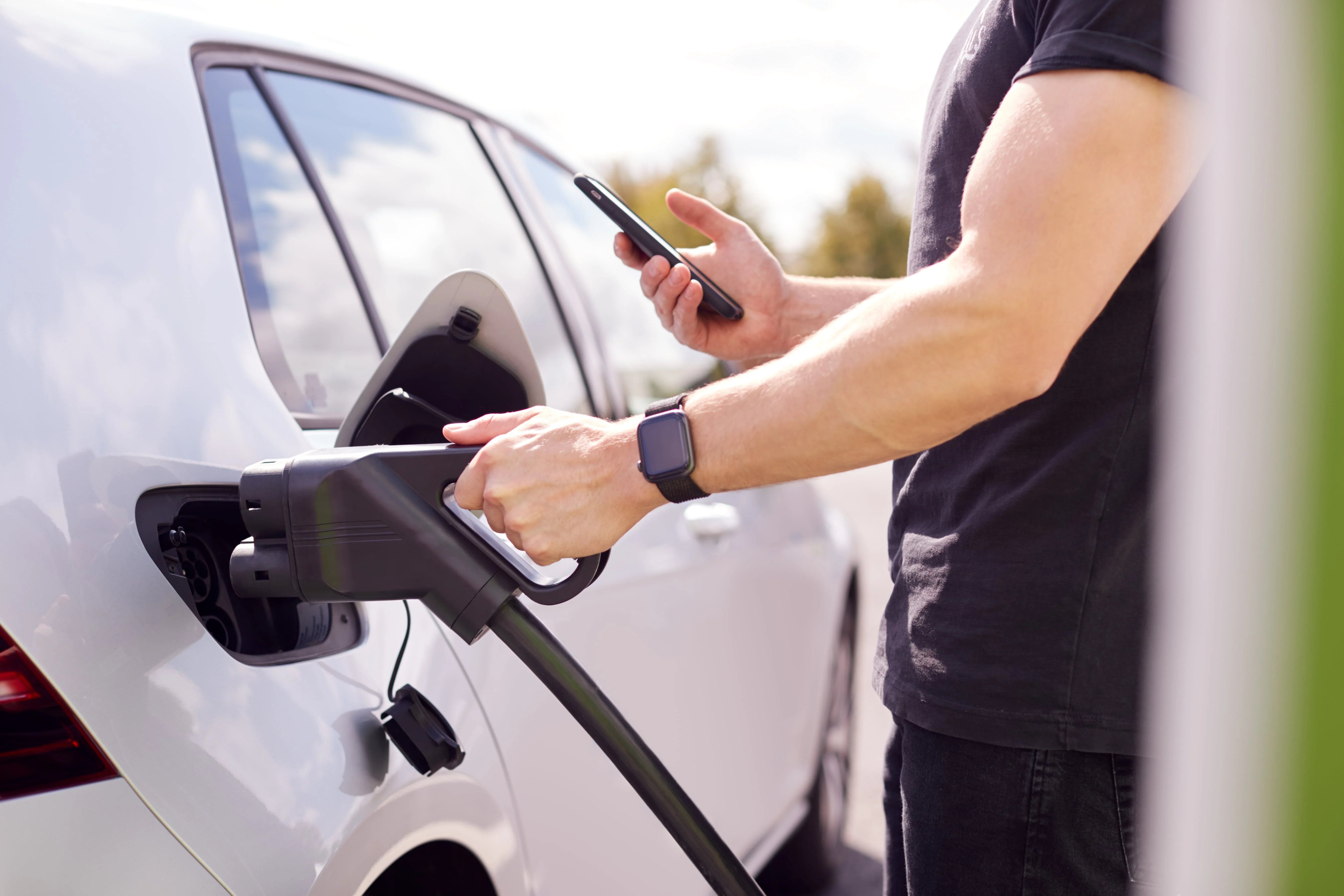 Someone plugging in their fast charging cable into a car, and authenticating the session on their smartphone.