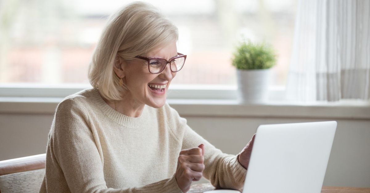 Woman sitting with a laptop and cup on a table smiling