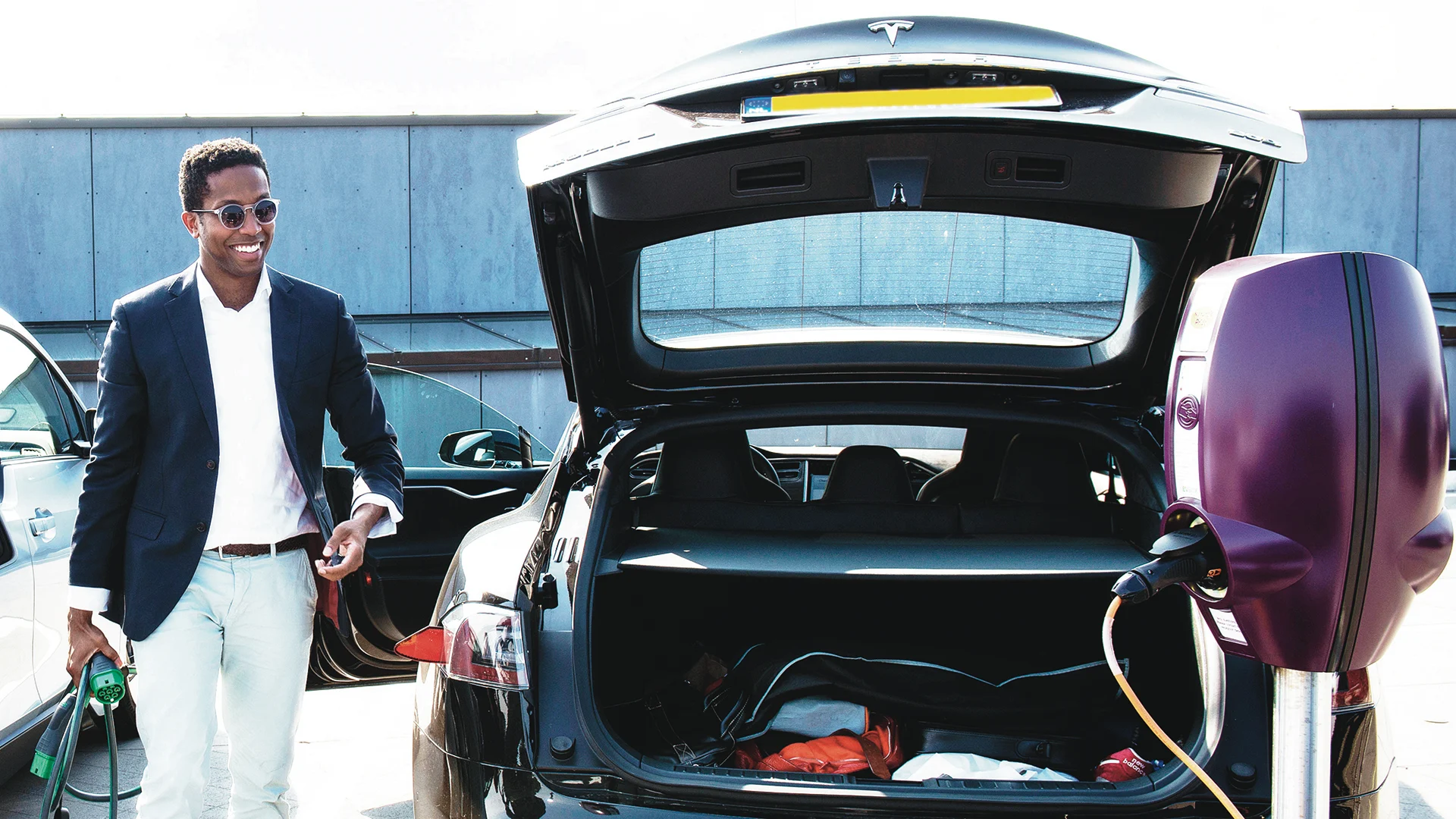 A young professional man about to plug his Tesla into a charging station in an office car park.