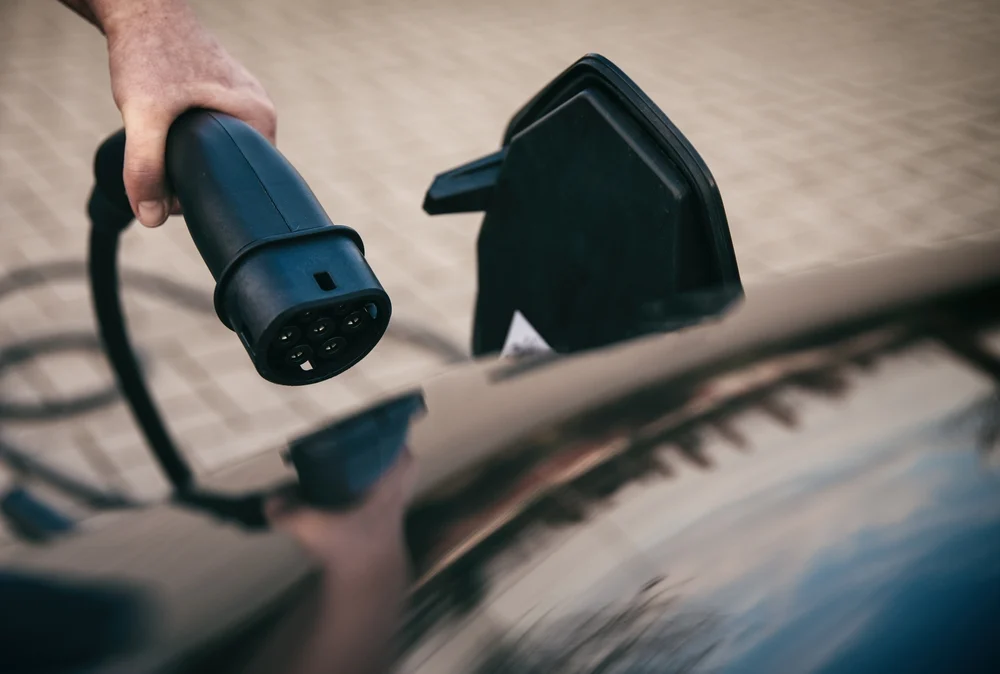 A hand holding a charging cable and in the action of plugging it into an electric car.