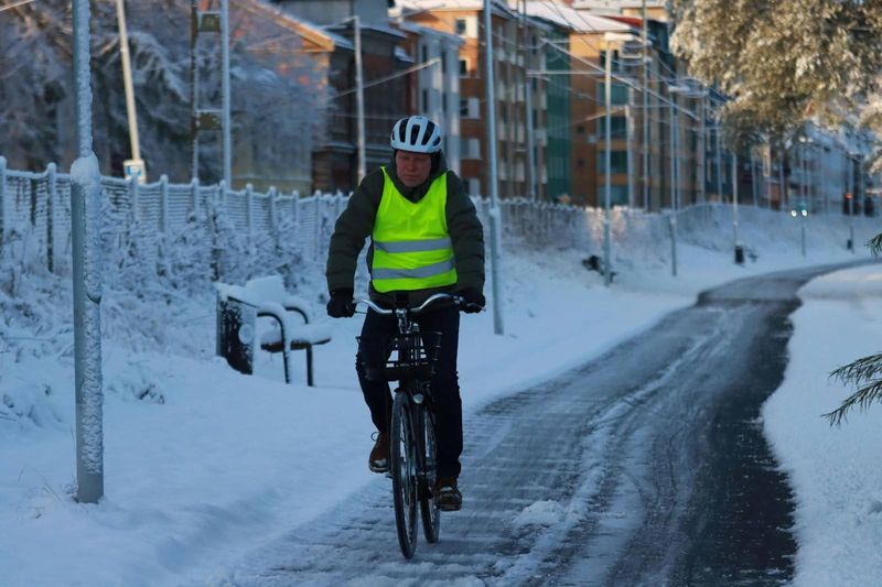 A man cycling on a snowy cycle path wearing a reflective jacket