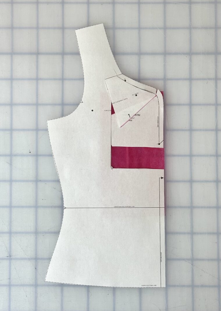 Front bodice pattern piece with a rectangle drawn around the center front neckline. The rectangle has been shifted upward. The top of the rectangle has been angled to blend with the original neckline. Pink paper has been placed under the open areas caused by shifting the rectangle.