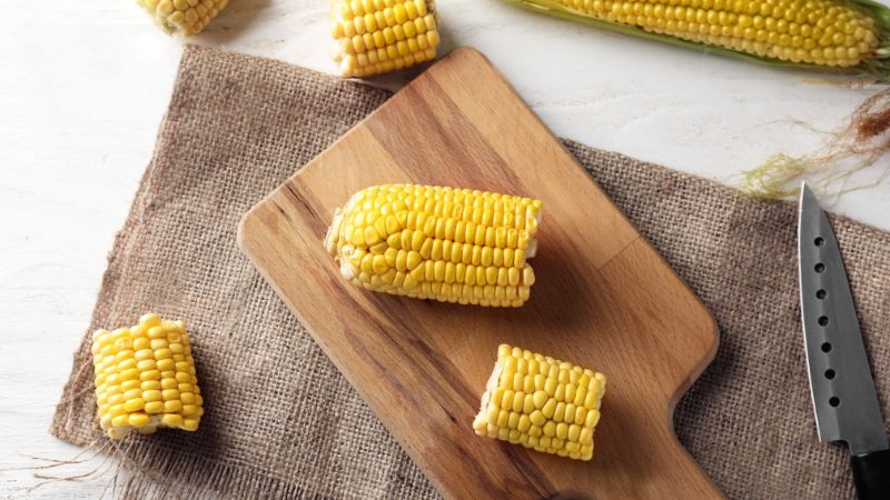 Pieces of corn cobs on a wooden board with a nearby knife, all atop burlap cloth.