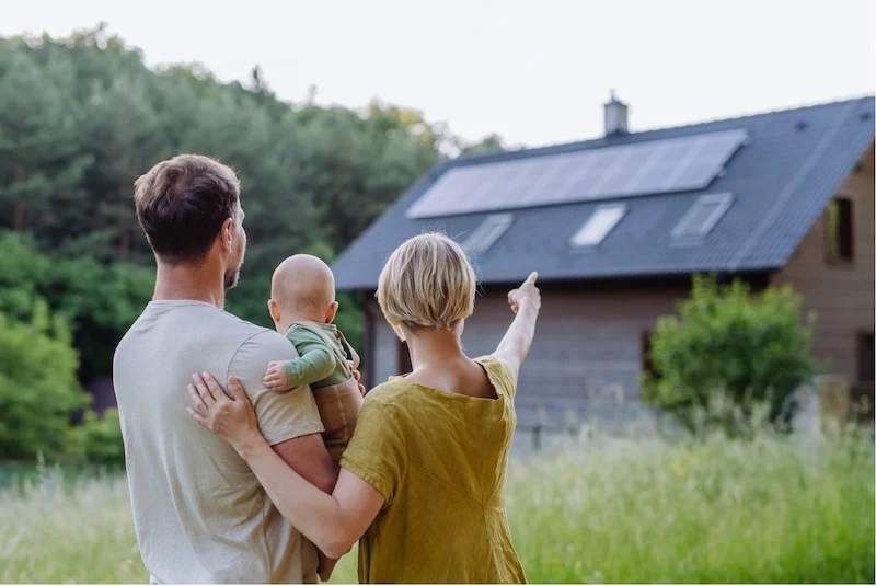 A family of three are looking at the solar panels installed on their house.