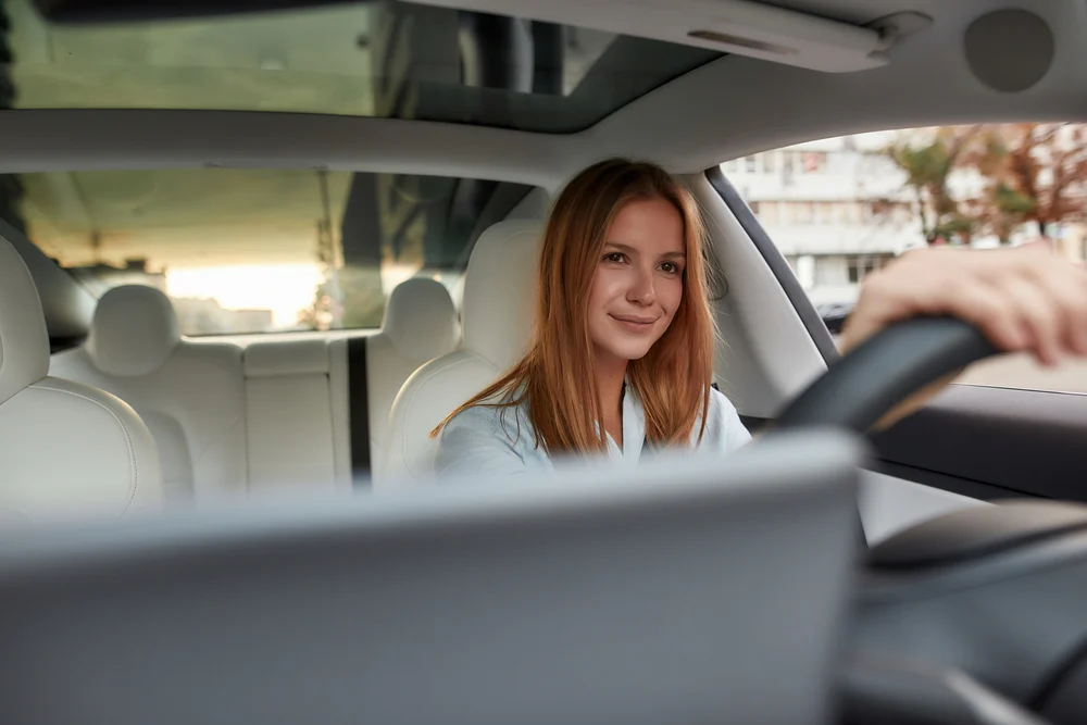 A young lady driving an electric car on a sunny day.