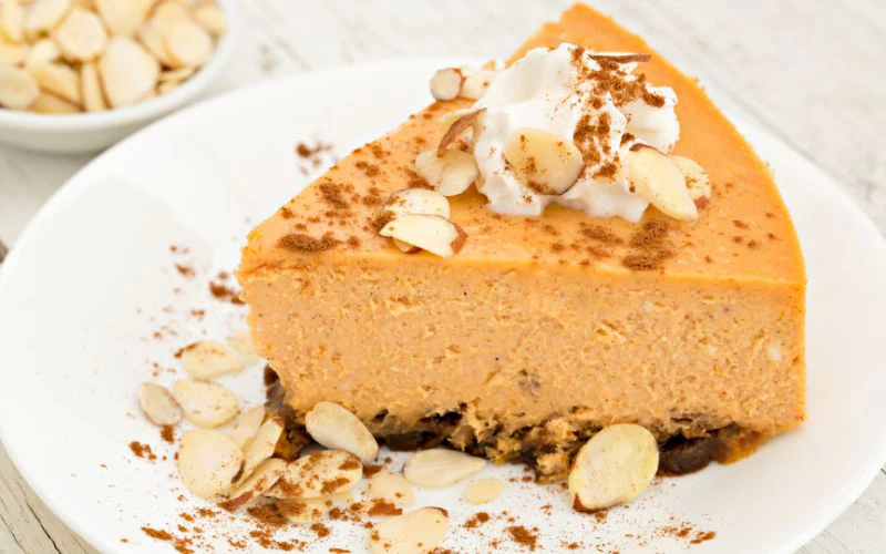 A creamy dessert slice with whipped cream, almond slices, and spice on a white plate.