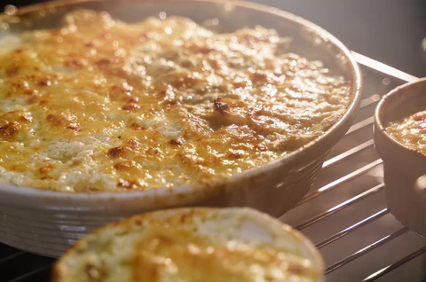 Baked scalloped potatoes in a white ceramic dish, fresh from the oven, golden and bubbling, with visible crusty edges.