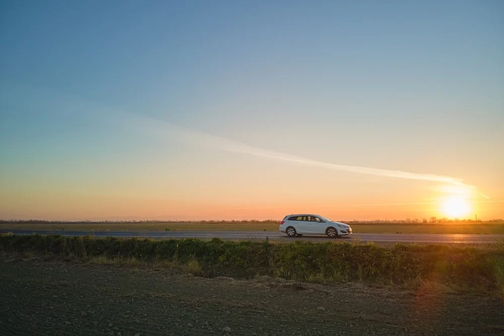 A white car driving on a scenic highway at sunset.