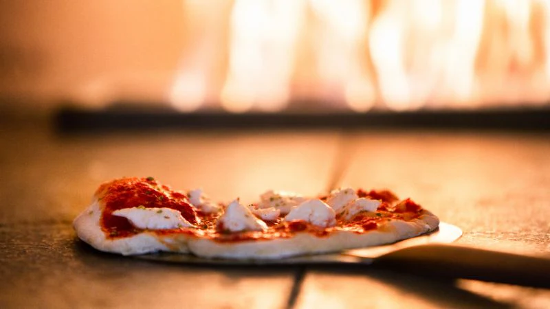 A homemade pizza with tomato sauce and cheese cooking in a wood-fired oven.