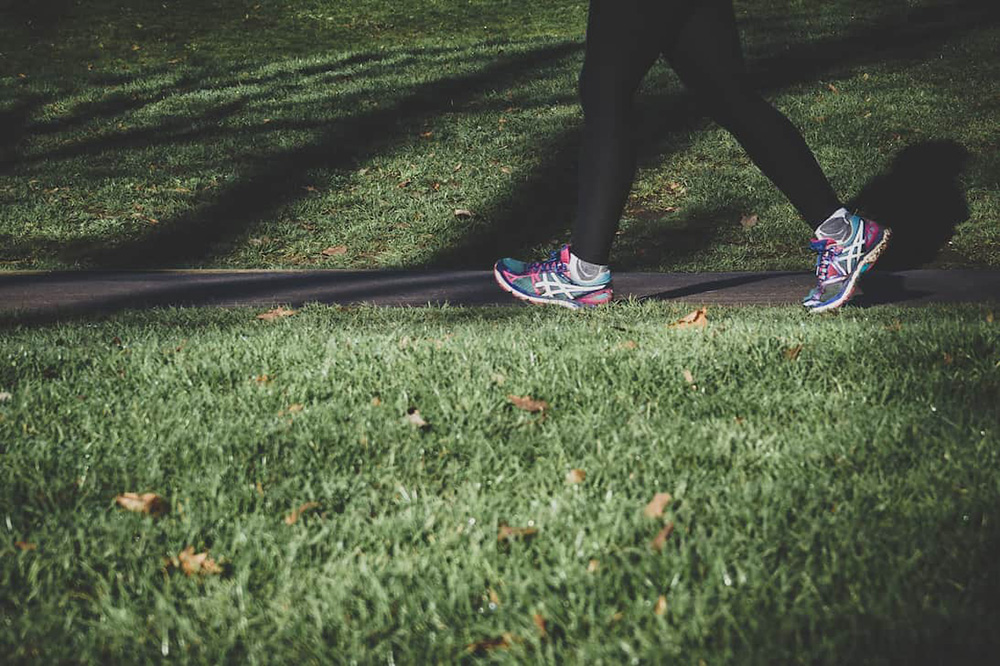 A close-up of a womanâ€™s running shoes jogging through a park