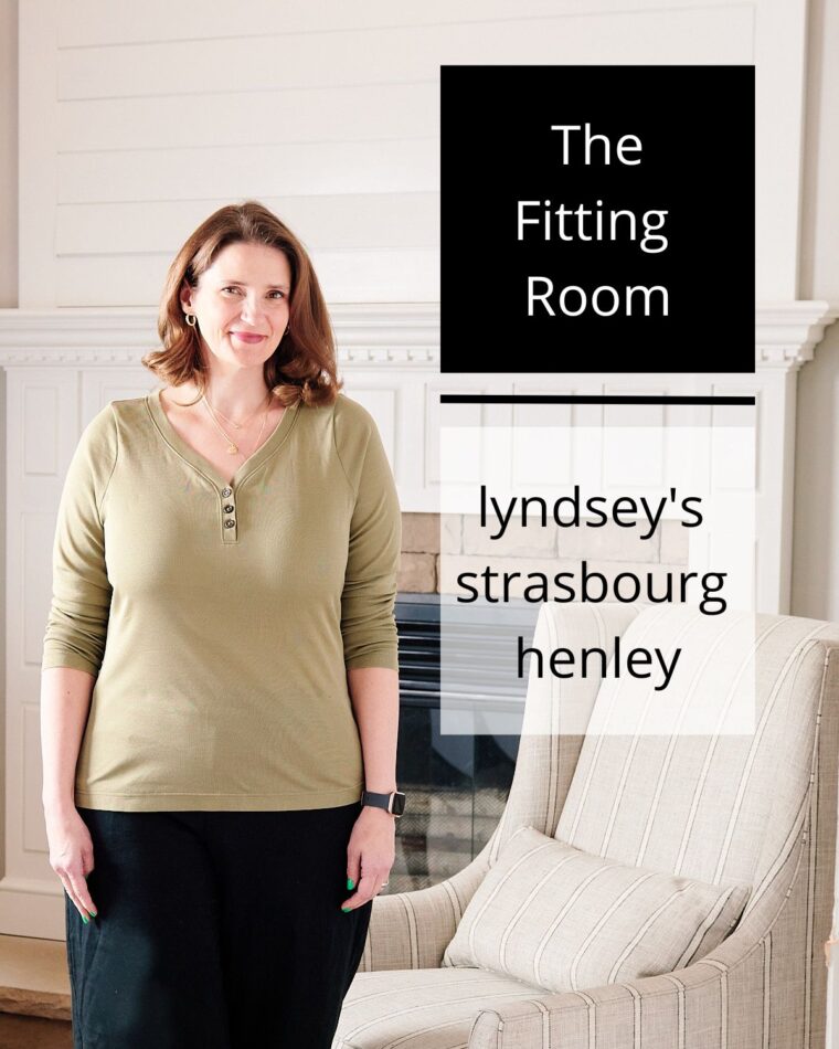 A woman wearing an olive-colored Henley standing near a fireplace. The image includes text reading 'The Fitting Room: Lyndsey's Strasbourg Henley'