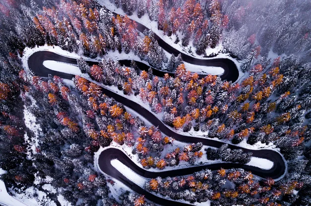 An aerial shot of a snow-lined highway in the forest in winter.
