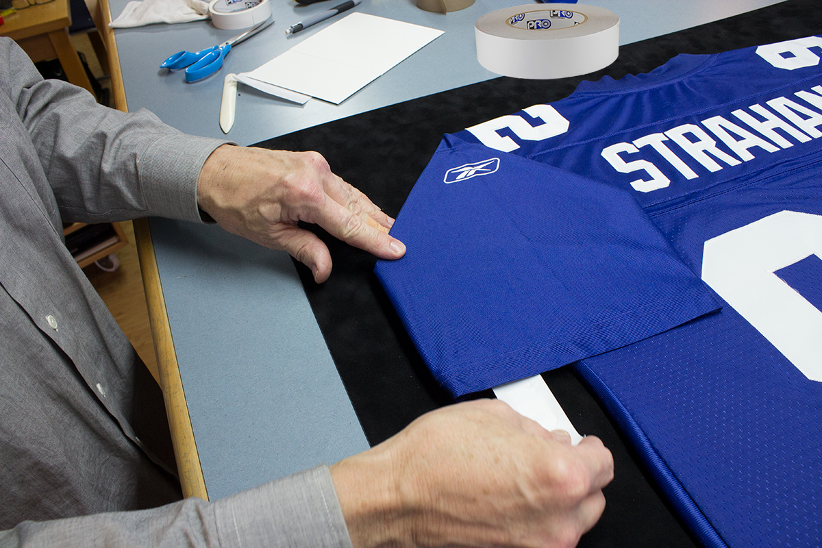 Our framer shown using ProÂ® Stitchery Tape to secure the sleeve of a jersey as he removes the tape liner to make the final bond.