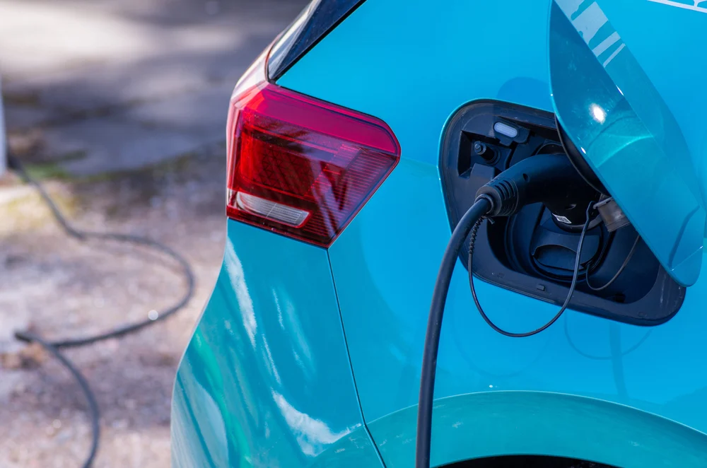 A closeup of a blue electric car that is plugged in and charging on a driveway
