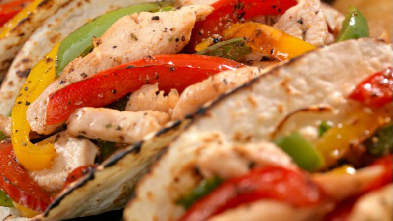 Close-up of pizza with grilled chicken, tri-color bell peppers, and black pepper seasoning.