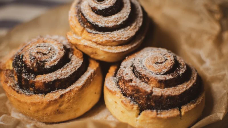 Three warm cinnamon rolls dusted with powdered sugar on parchment.
