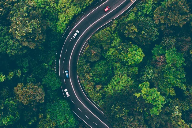 An aerial shot of a winding three-lane highway in the forest.