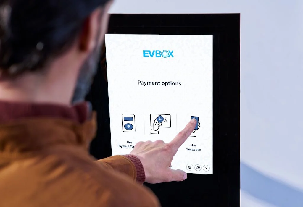 A man selecting a payment method on the touch screen of an EVBox Troniq High Power charging station.