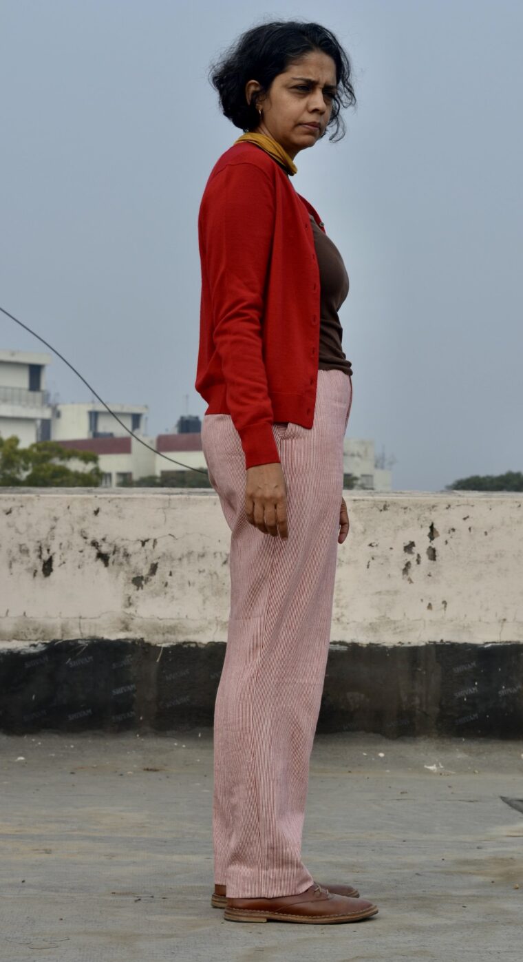 A side view of a woman standing in red and white trousers paired with a brown sweater and a red cardigan.