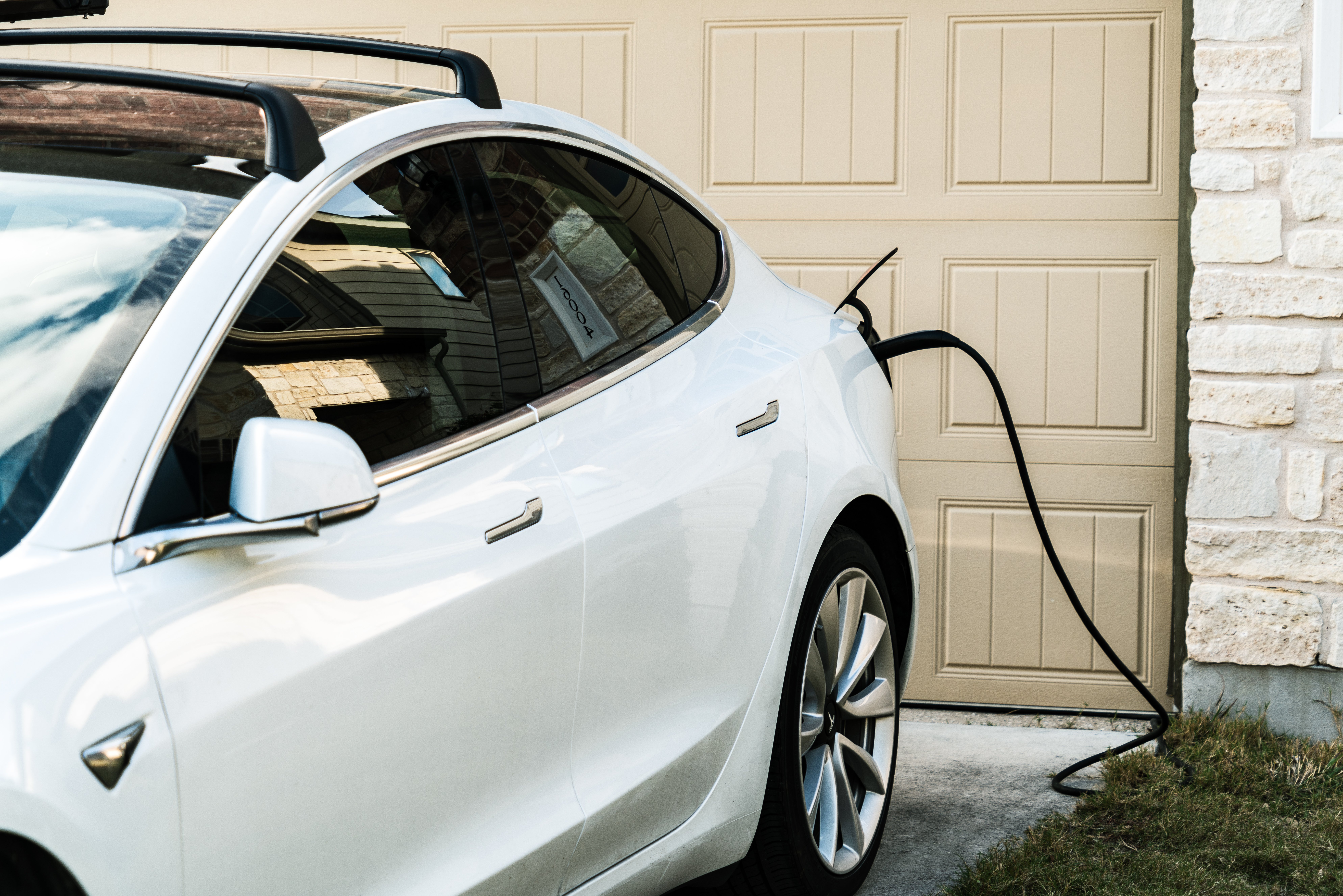 A closeup of a white car charging at home outside a garage