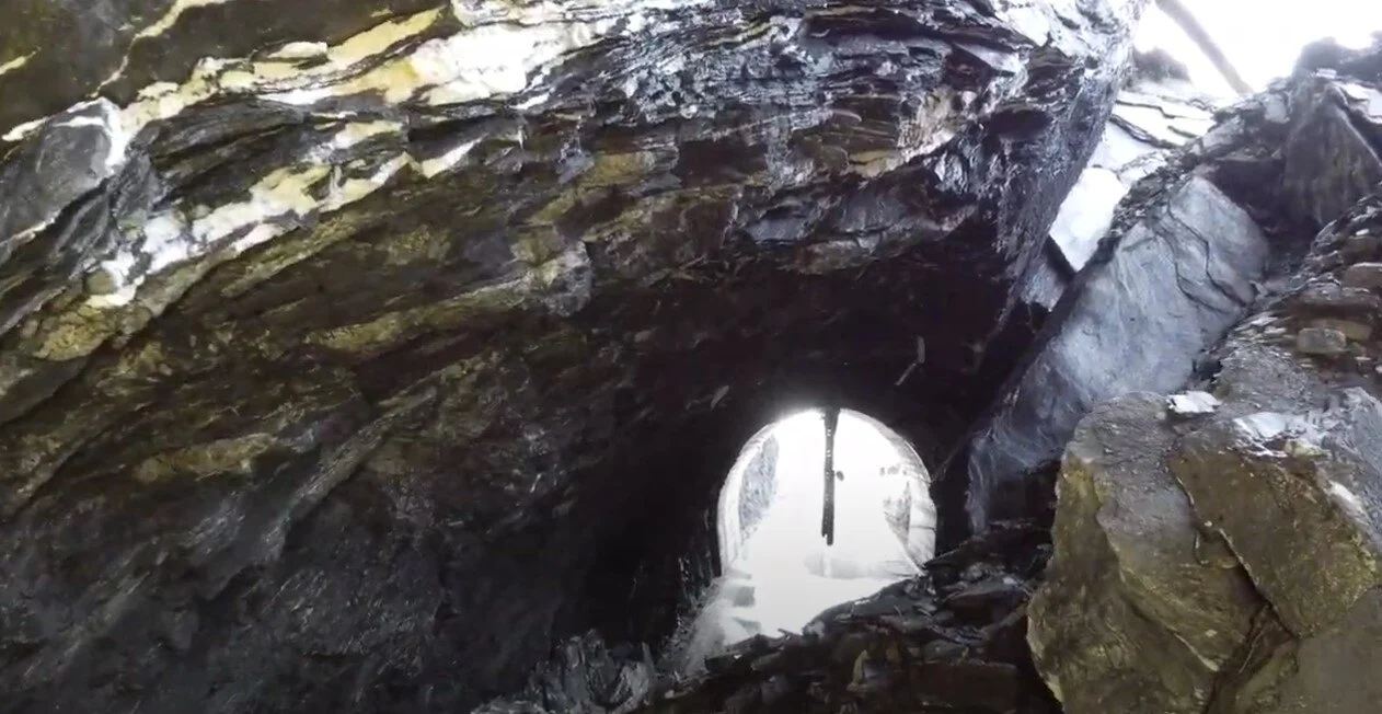 Photo of rocks piled high in side the collapsed tunnel, with tunnel opening visible beyond rockpile 