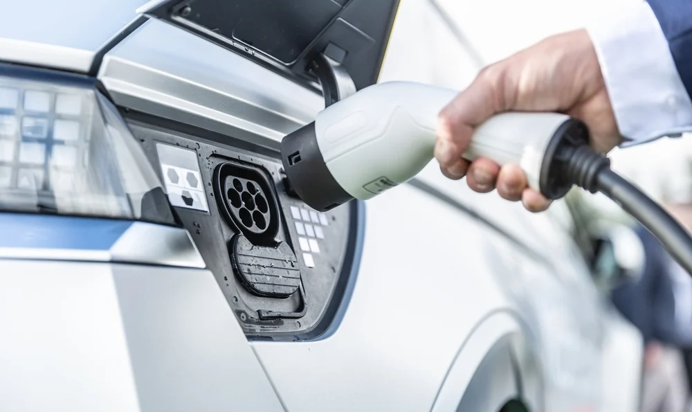 A man holding a charging cable in the action of plugging it to his electric car.