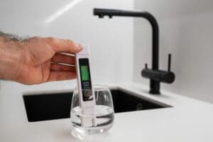 Man hand immerses TDS tester into the water in glass. demonstrates that the water is clean employee performing water test at work