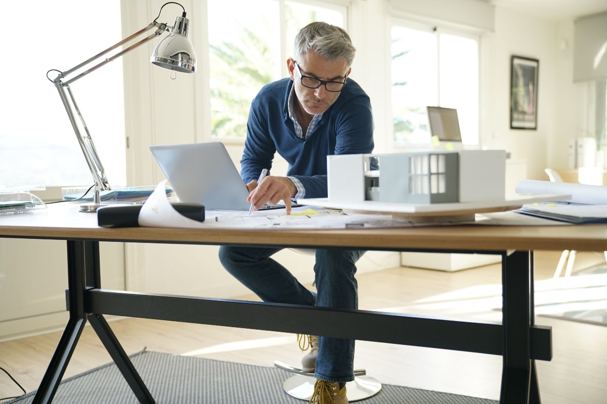 Architect sitting on a stool while reviewing blueprints, showcasing the height and flexibility of drafting stools for design work.