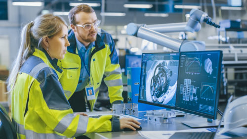 At the Factory: Male Mechanical Engineer and Female Chief Engineer Work Together on the Personal Computer, They Discuss Details of the 3D Model