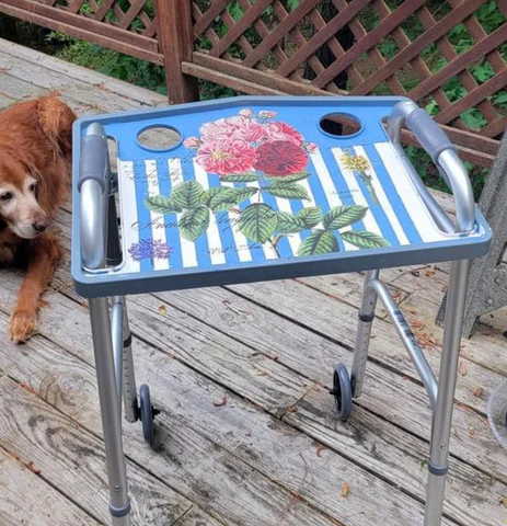 A silver walker with a tray that has been decorated with a design of blue and white stripes and a pink flower