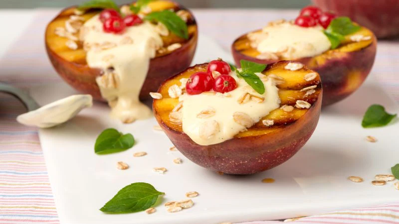 Grilled peach halves with cream, red berries, granola, and mint on a white plate.