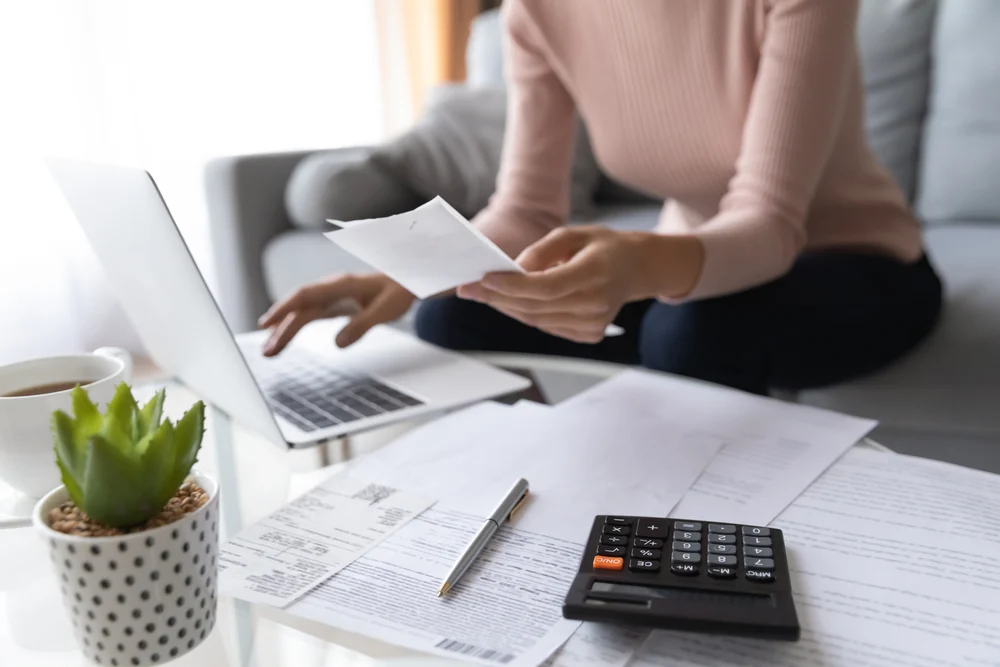 A woman is checking some energy bills with a laptop and a calculator.