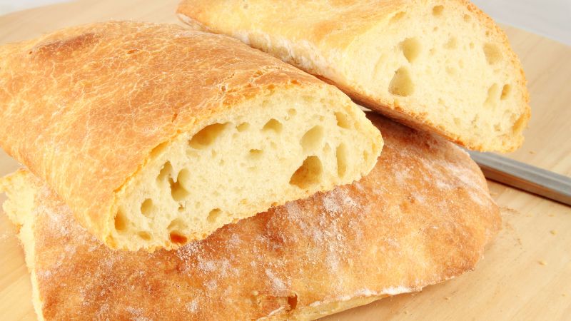 Sliced ciabatta with a golden crust and airy interior on a wooden surface.