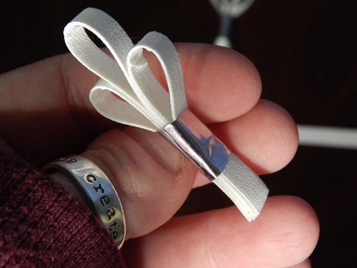 I hand ripped strips of Â¼â€ white ProÂ® Gaff tape. I married 2 pieces together. Then I took 3 married strips, bent them each over individually, creating a loop and combined them together like a tiny bouquet, then I secured them together by wrapping a piece of silver ProÂ® Sheen around the stem of the â€œbouquetâ€.