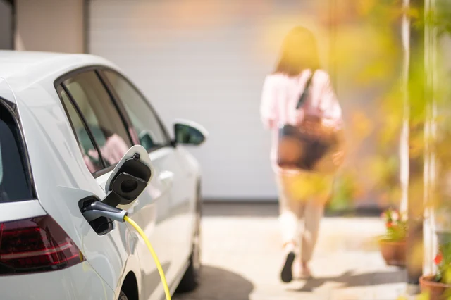 A closeup of a car charging outside a garage on a sunny day