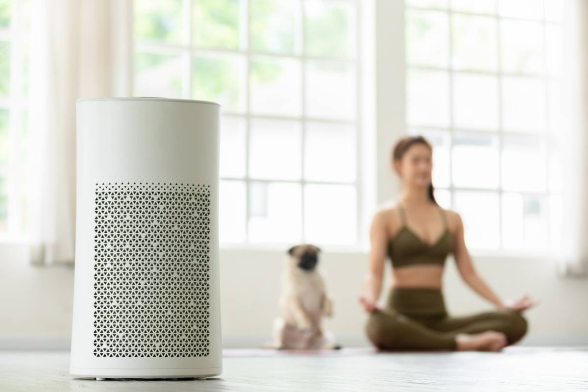 A woman meditating with her dog in a bright room, with a white air purifier in the foreground, highlighting the Health Benefits of Air Purifiers for Dogs