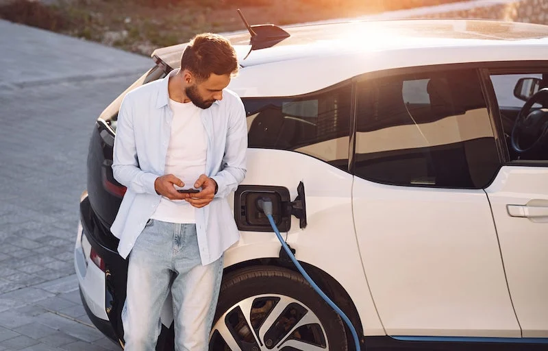 A man is waiting for his EV to be charged while holding on his phone.